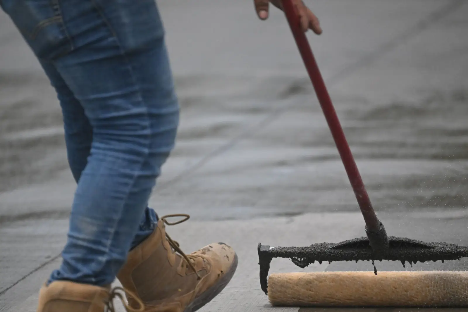 Worker drawing a roller applicator across a concrete surface to apply sealer