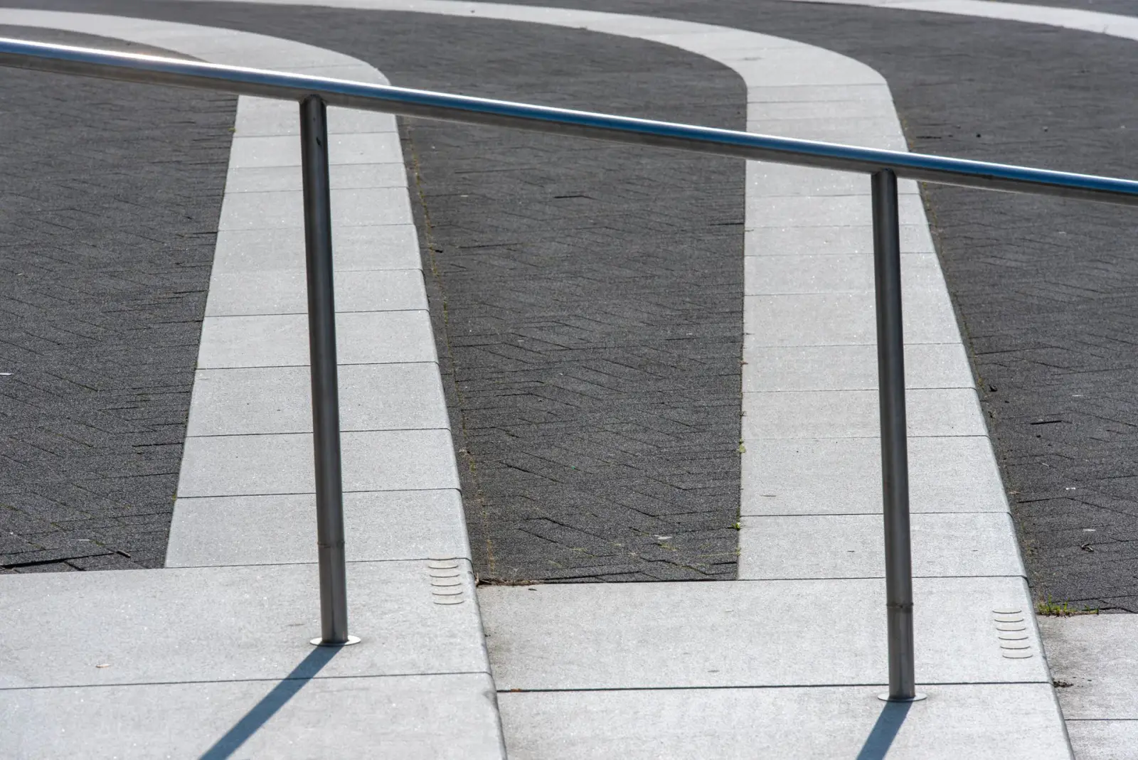 Light-toned concrete walkway panels flanked by a metal handrail on a commercial property