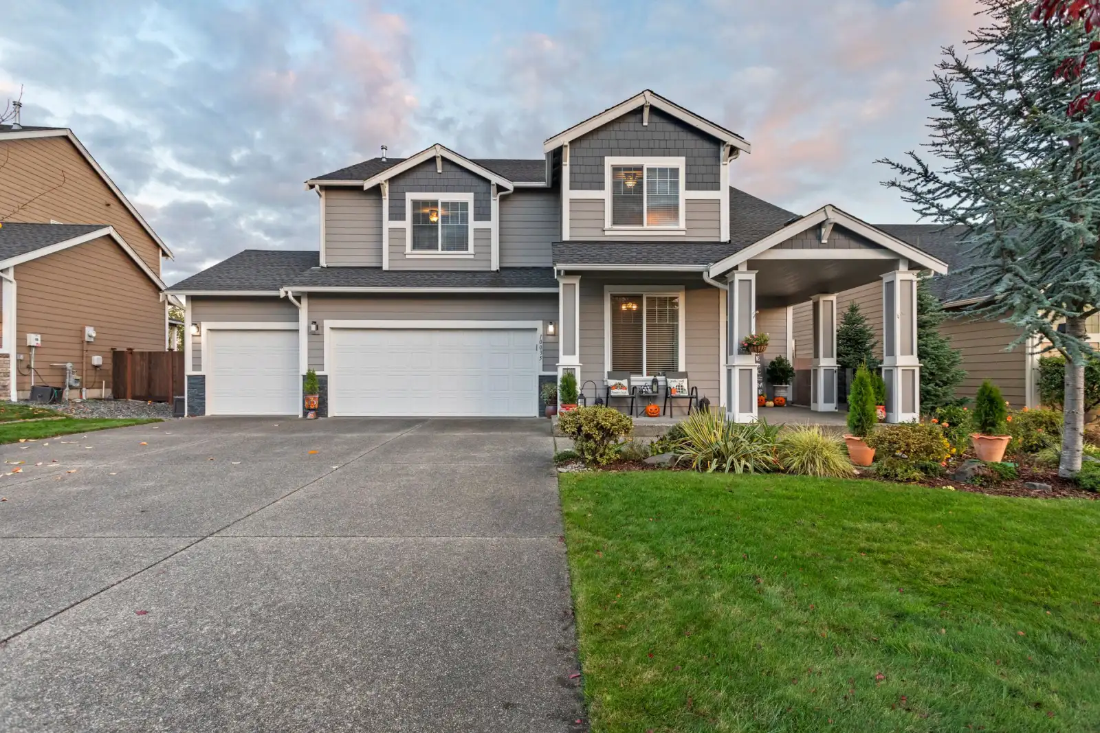 Two-story home at dusk with a wide concrete driveway running to a three-car garage and a concrete front walk