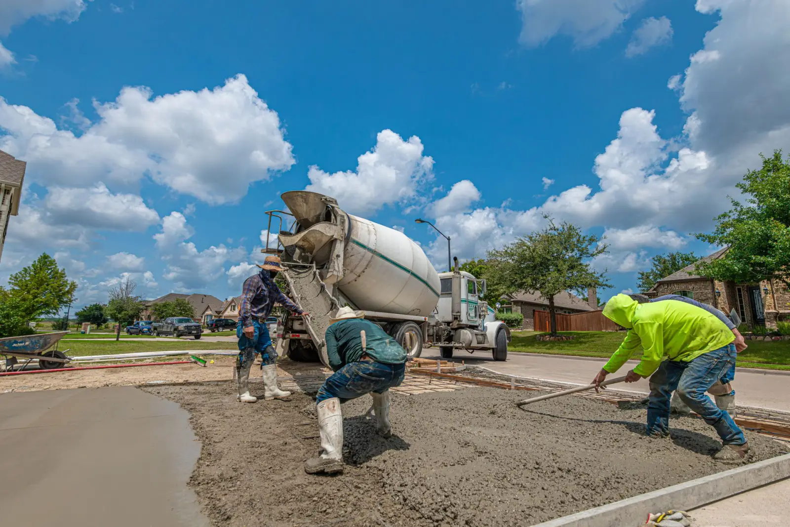 Ready-mix truck discharging while two workers rake and screed a fresh concrete driveway pour