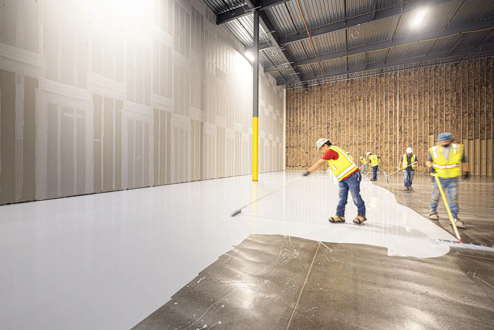 Crew in high-visibility gear placing and levelling a large concrete floor slab inside a building