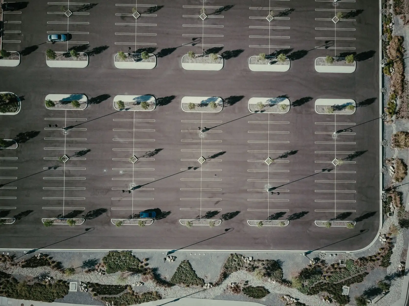 Aerial view of a parking lot with marked stalls and parked cars beside a commercial building