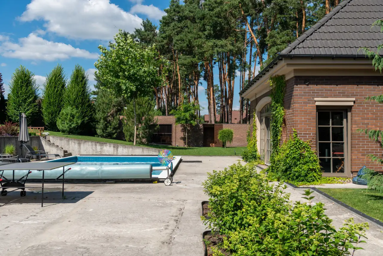 Brick house with a broad light-grey concrete patio and pool deck surrounded by pines