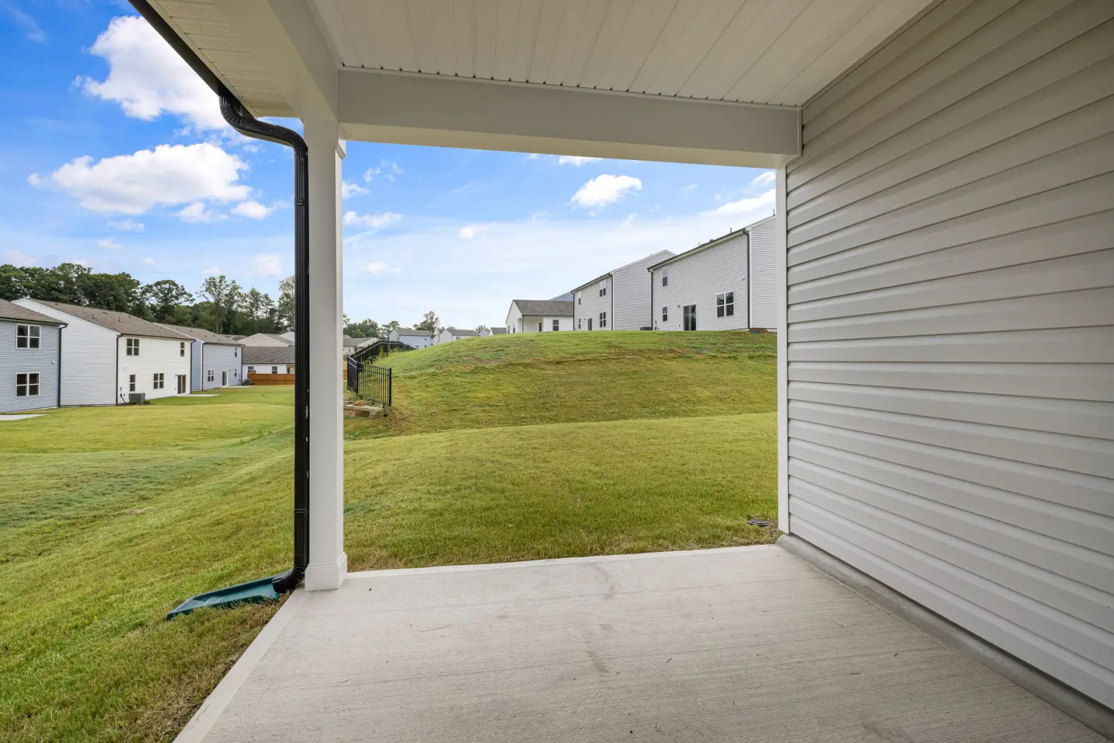 Covered concrete patio slab under a house overhang looking out across a green lawn