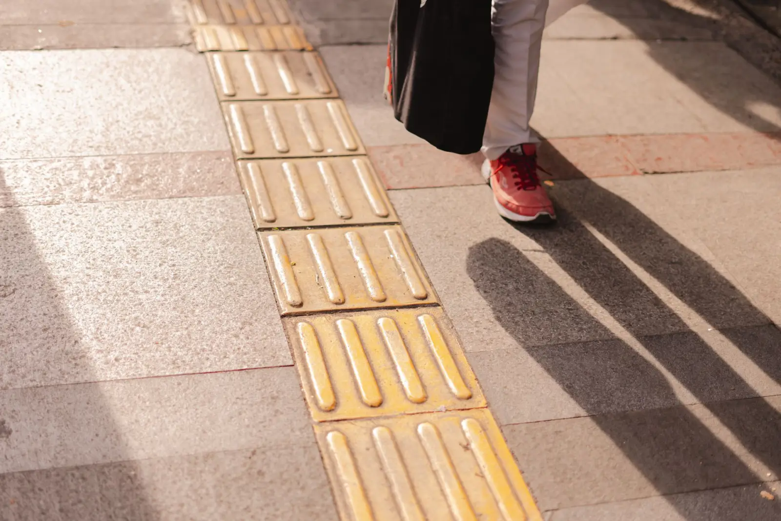 Detectable warning surface with raised truncated domes set into a concrete walkway as a pedestrian passes