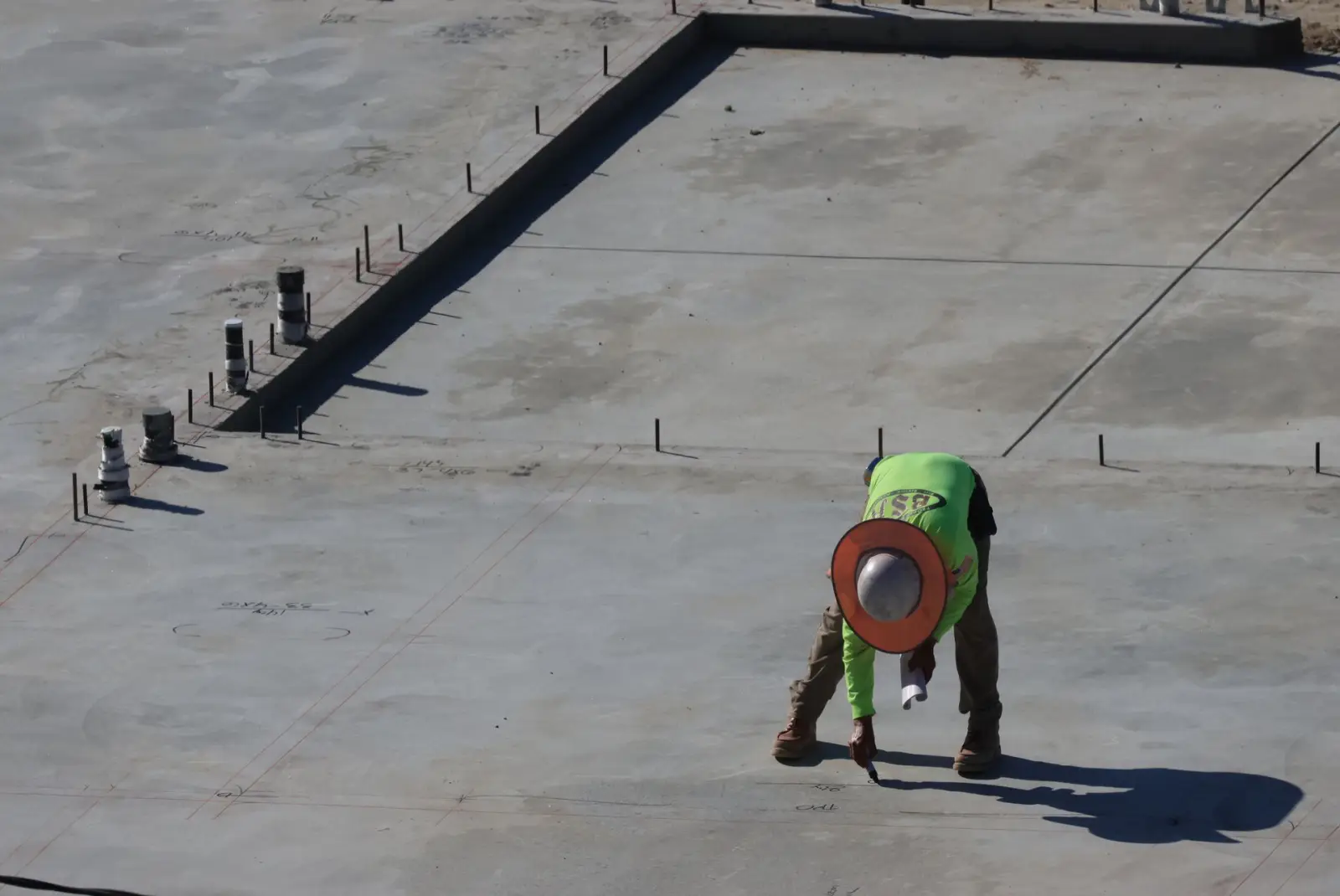 Worker in a hard hat and high-visibility vest working along the formed edge of a concrete slab