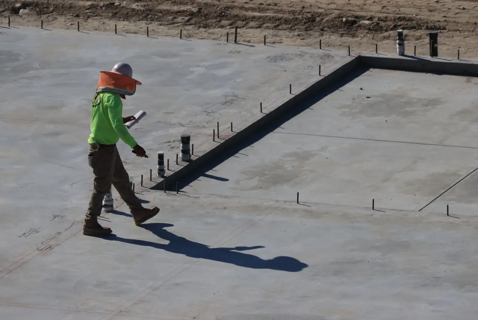 Formed concrete slab with dowel pins set along the edge, a worker walking the surface