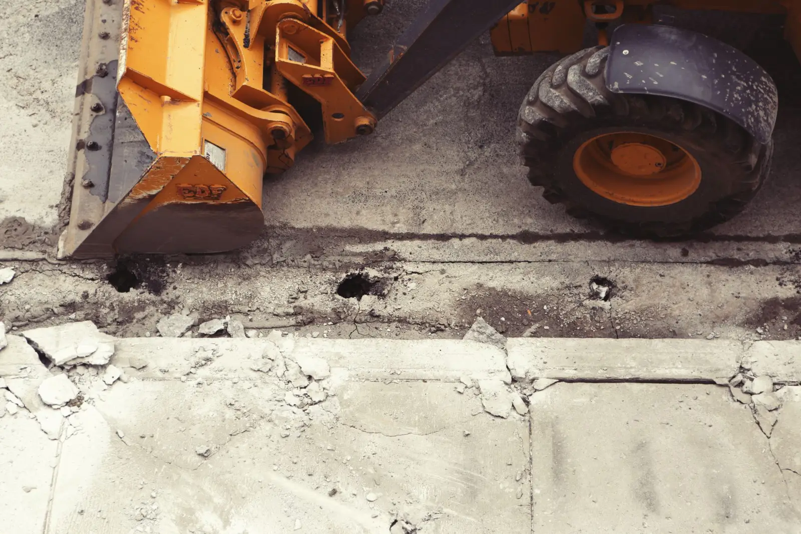 Loader bucket working across a broken concrete pavement surface during a removal job