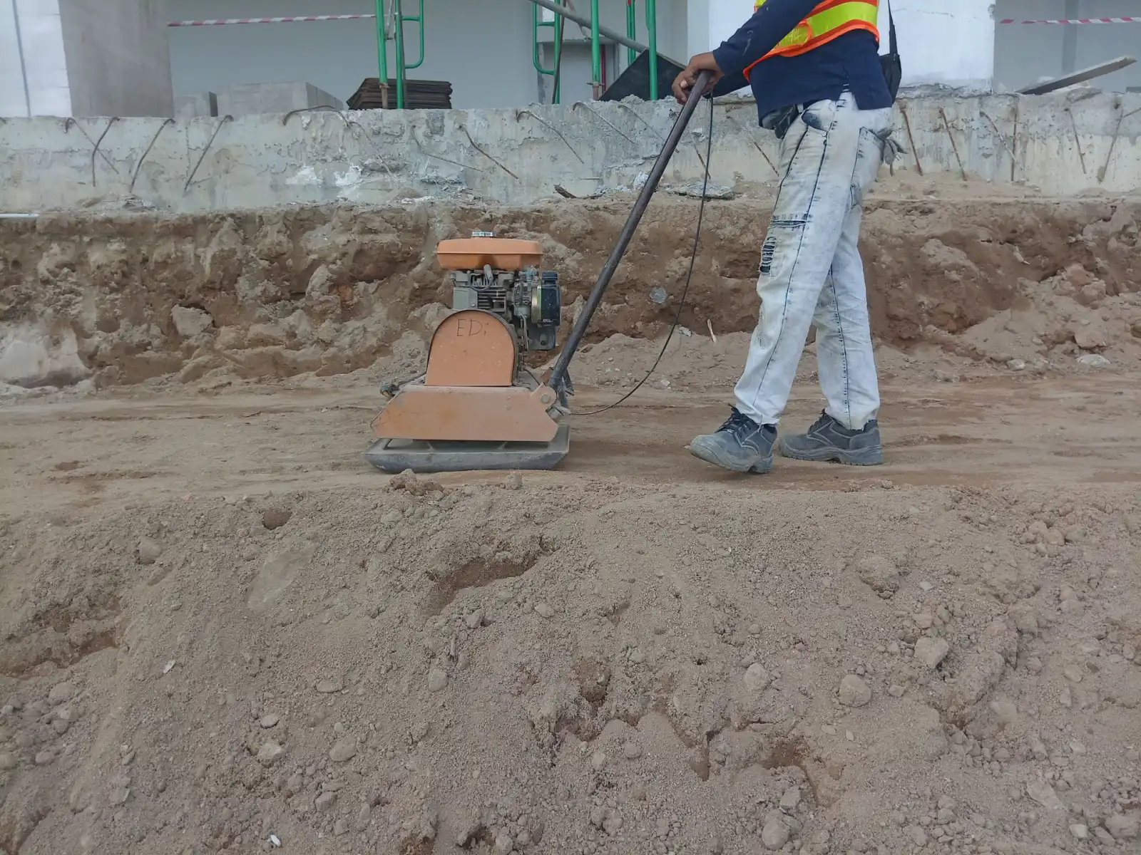 Worker running a plate compactor across subgrade soil during base preparation