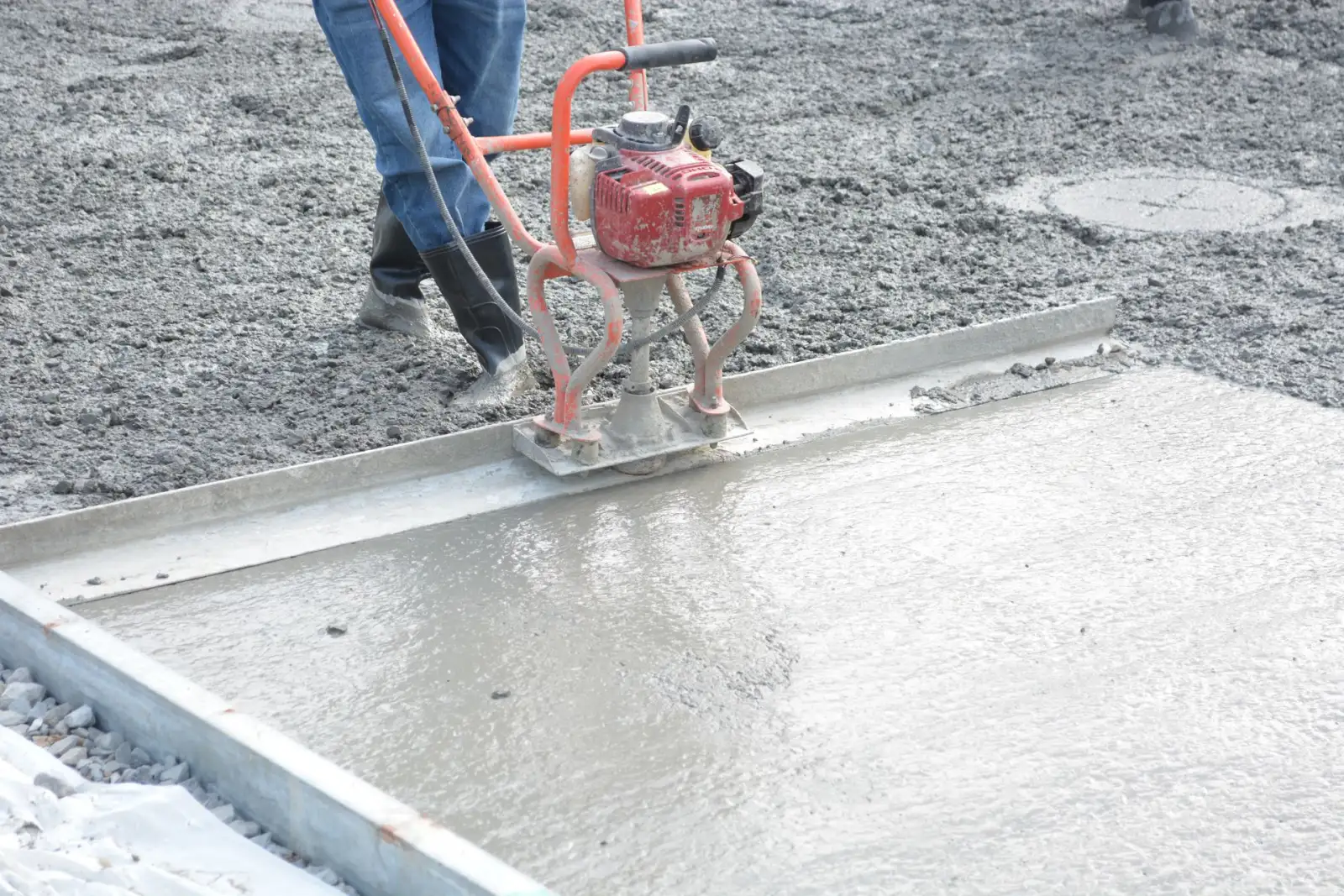 Power screed leveling freshly placed concrete between form boards on a slab pour