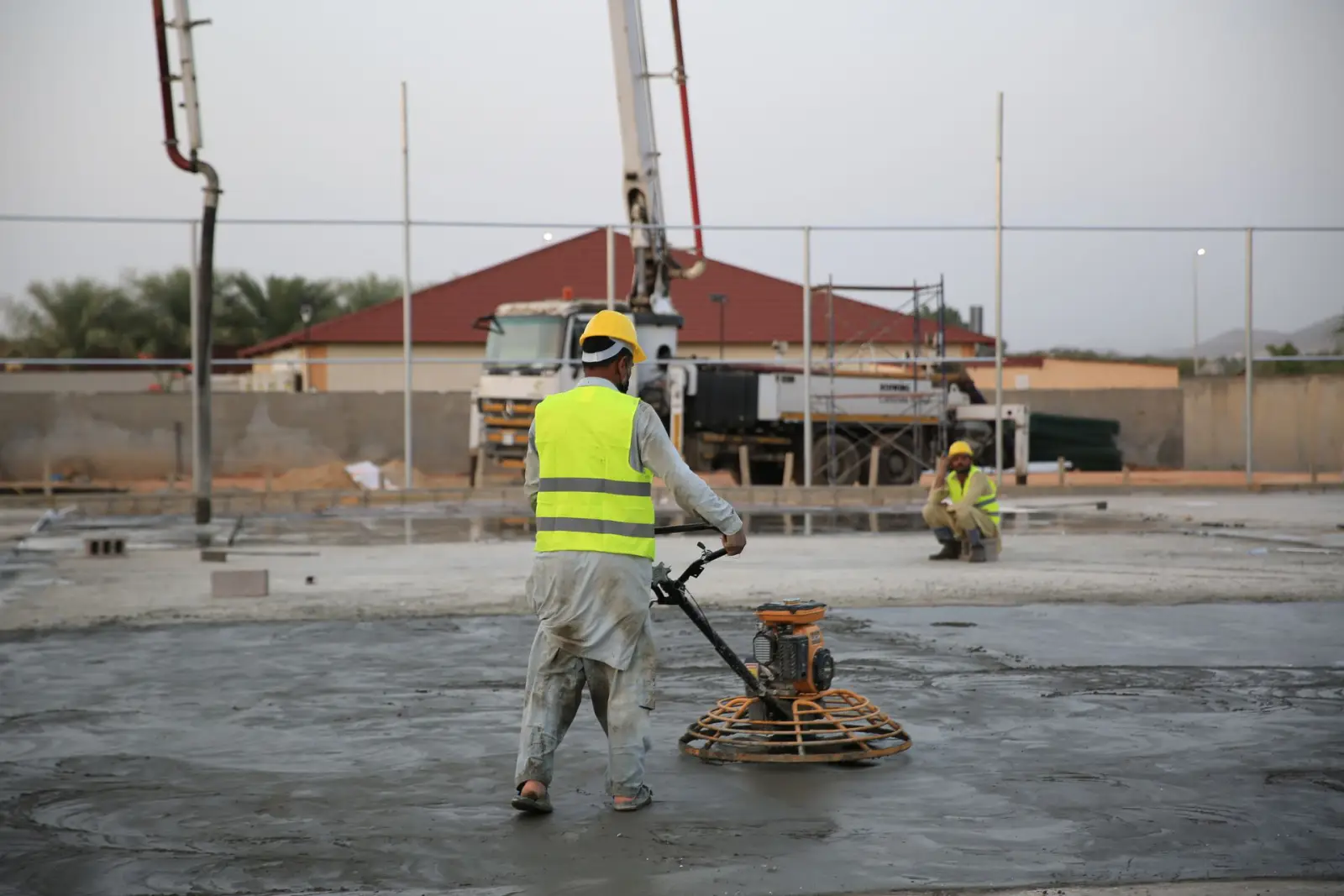 Worker running a walk-behind power trowel across a freshly placed concrete slab