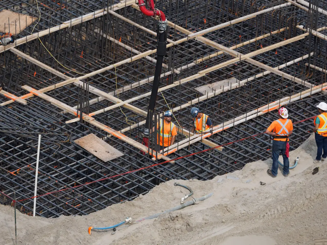Aerial view of a large reinforcing steel mat laid out over a commercial foundation with a crew and crane