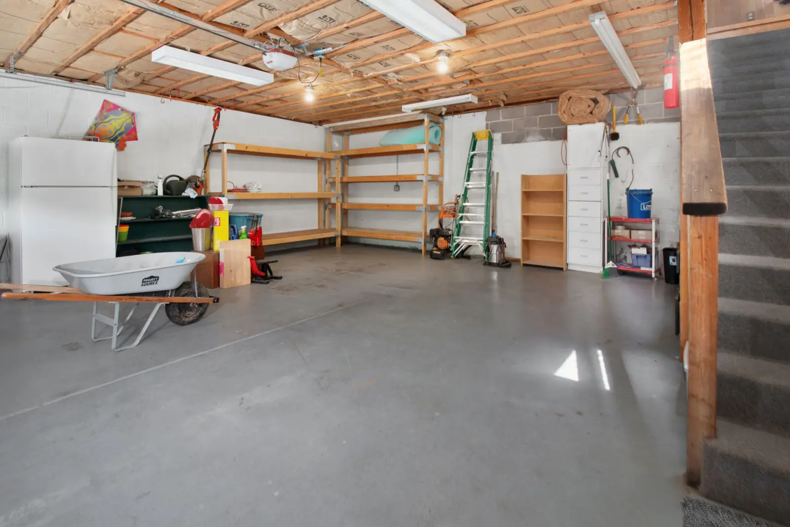 Residential garage interior with a smooth grey concrete floor, storage shelving and a wheelbarrow