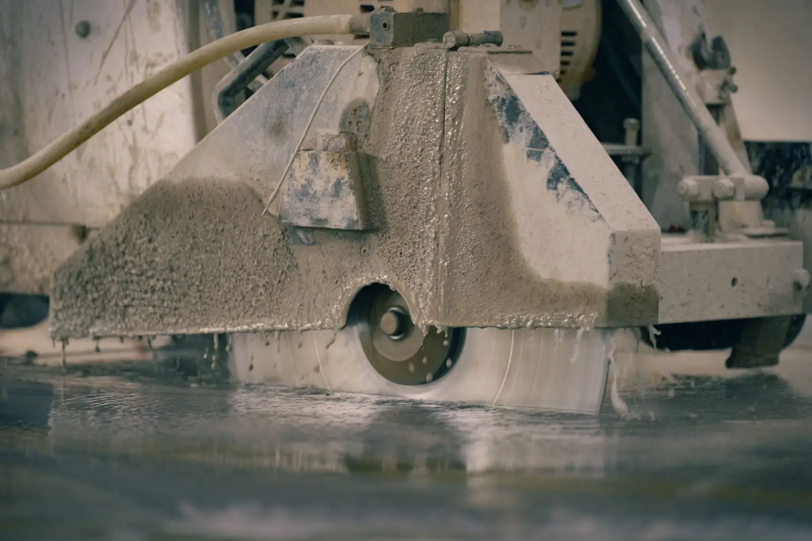 Concrete saw cutting a control joint into a cured slab, with wet slurry at the blade
