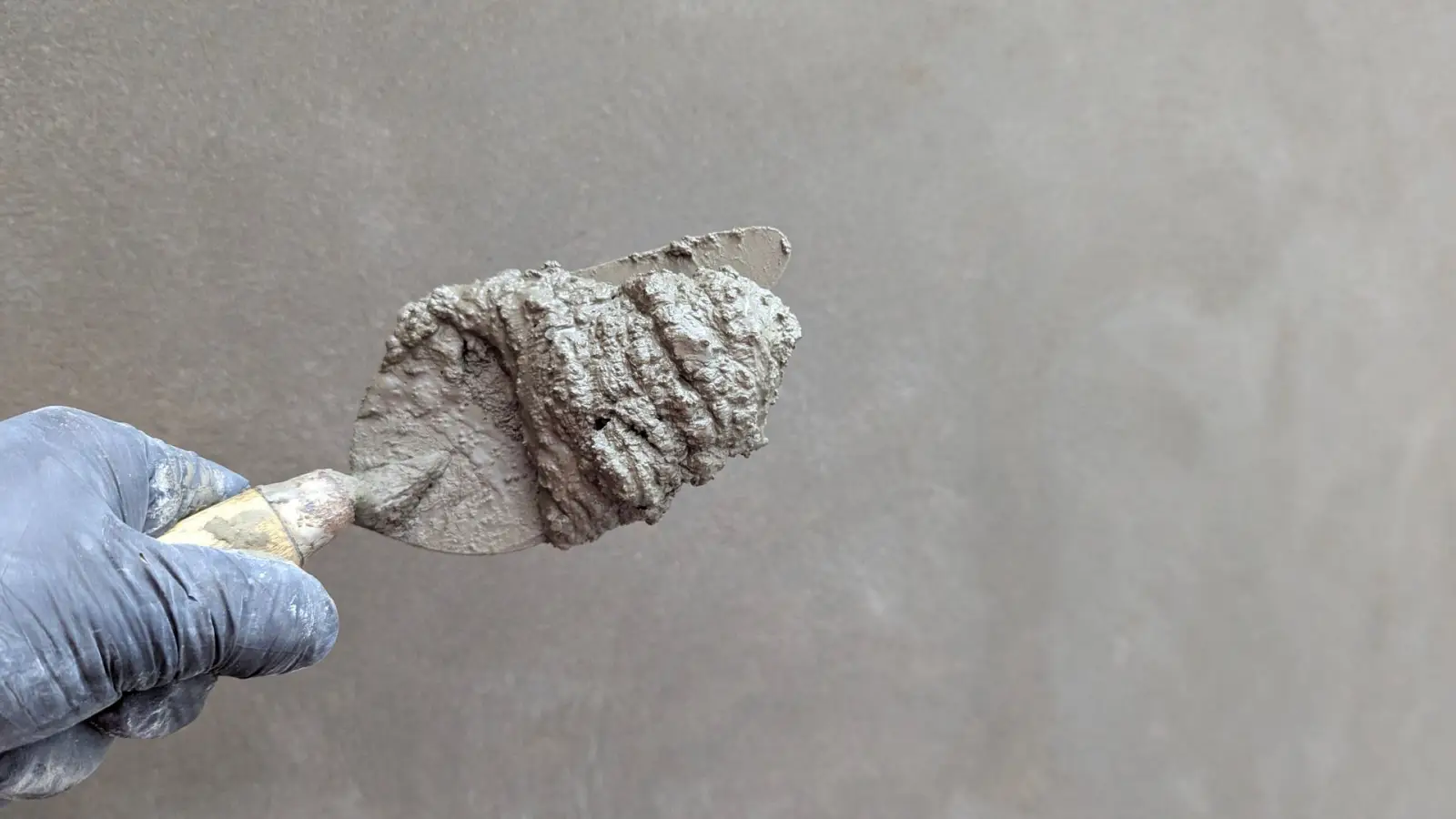 Gloved hand holding a trowel loaded with cementitious patch material against a concrete surface