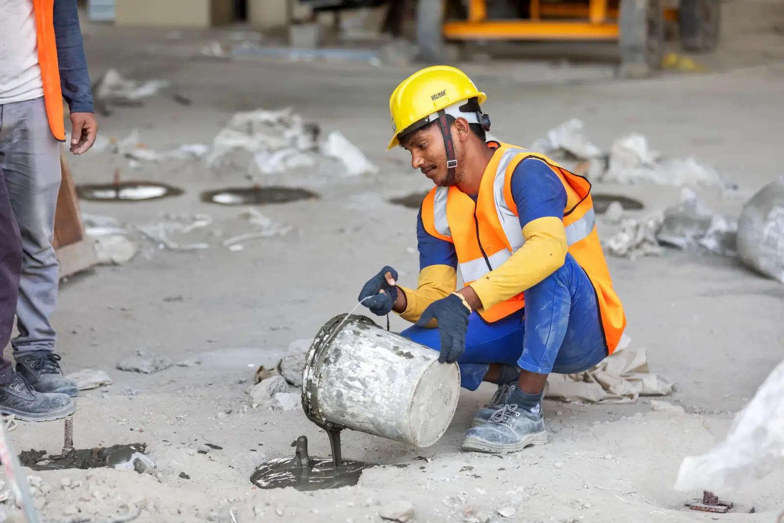 Worker in a hard hat and high-visibility vest placing repair material on damaged concrete